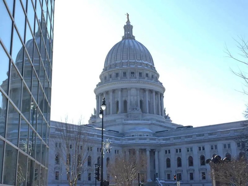 The state Capitol in Madison is reflected off the windows of an office building across the street. (Photo by Julian Emerson)