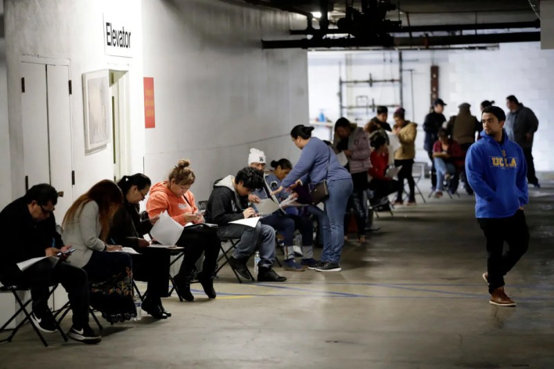 Hospitality workers wait in line in a basement garage to apply for unemployment benefits
