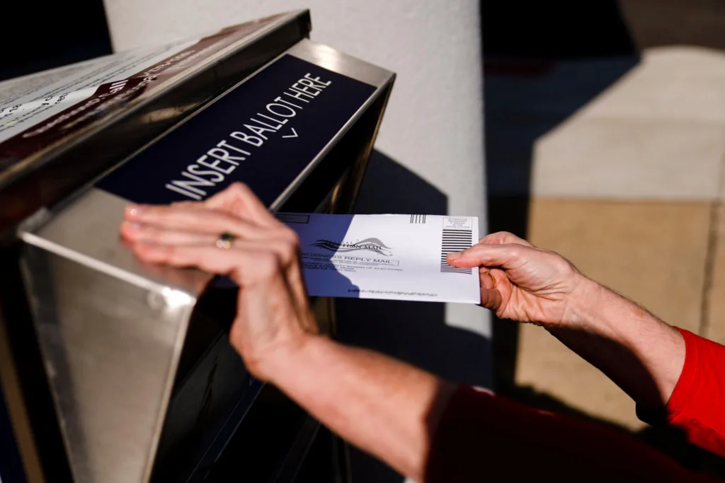 Voting - Photo of voter's hands dropping absentee ballot into ballot drop box