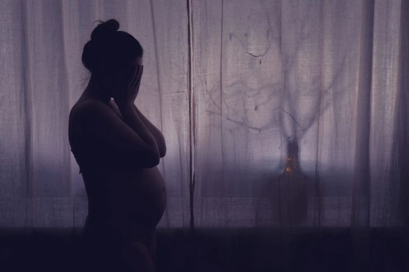 Young pregnant woman crying with her hands folded near her face.
