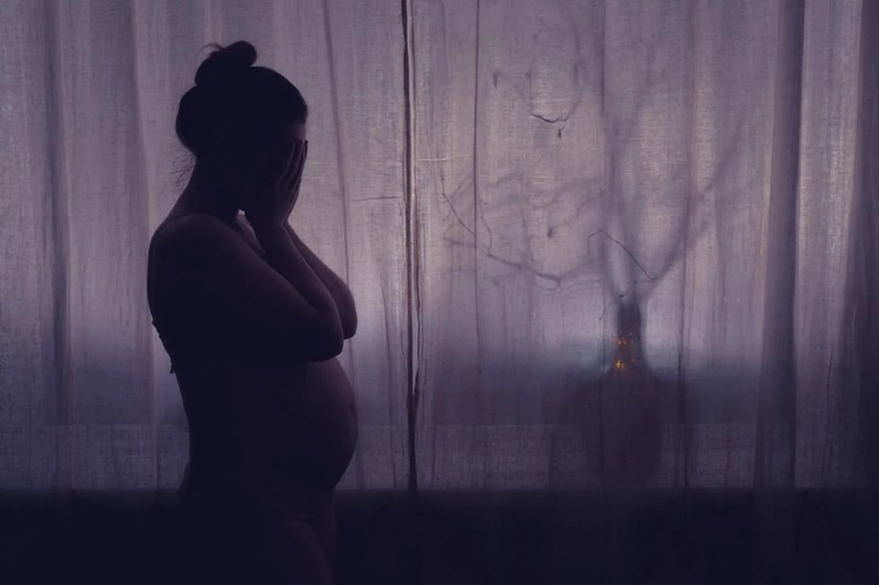 Young pregnant woman crying with her hands folded near her face.