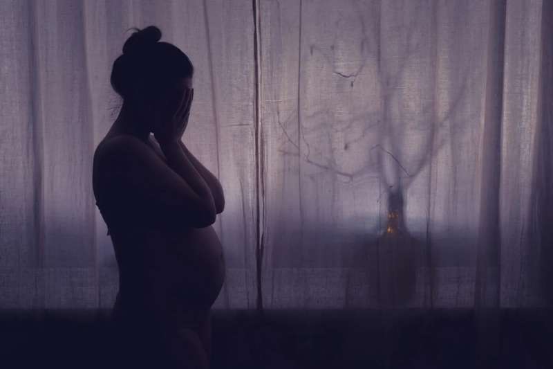 Young pregnant woman crying with her hands folded near her face.