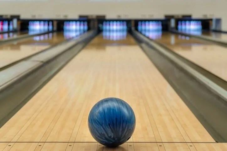 A blue bowling ball sits at the top of a bowling alley.