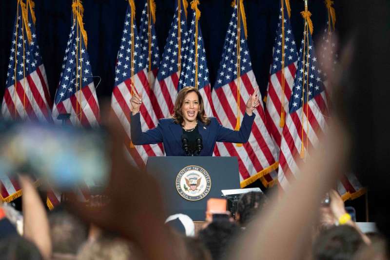 Kamala Harris on stage in Wisconsin raising her arms in cheer in front of american flags.