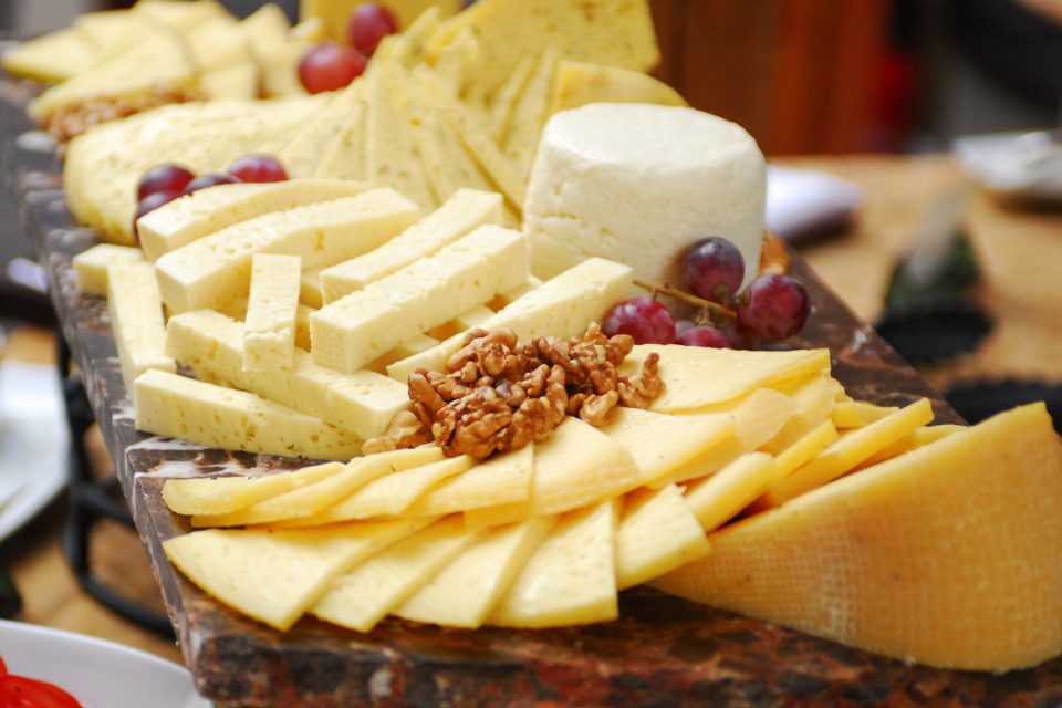 A variety of cheeses on a wooden board with fruit and nuts.