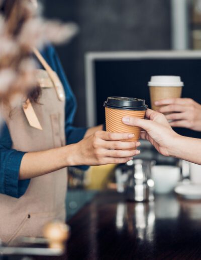 A barista handing a coffee to-go to a customer.