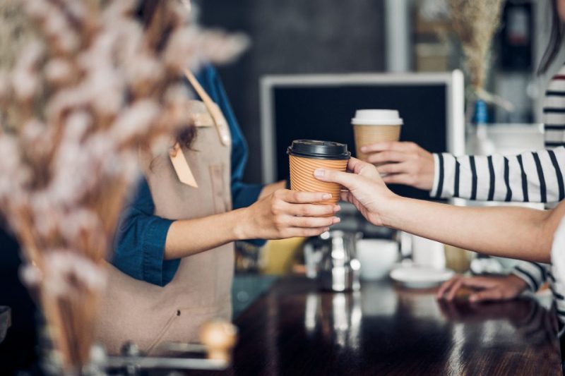 A barista handing a coffee to-go to a customer.