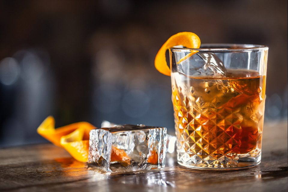 An old fashioned cocktail in a fancy glass with garnishes on the side.