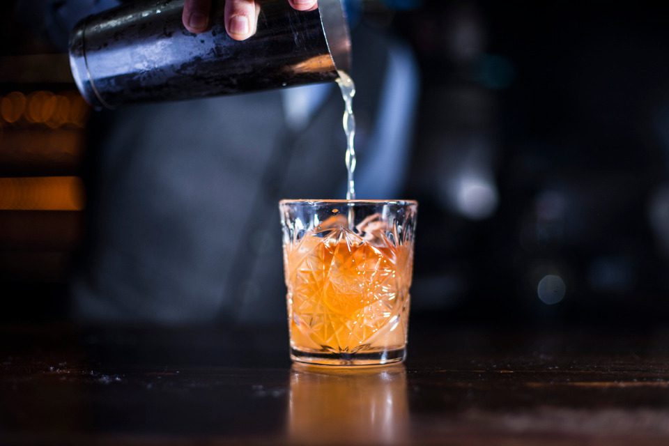 A bartender pouring an old fashioned from a drink shaker.