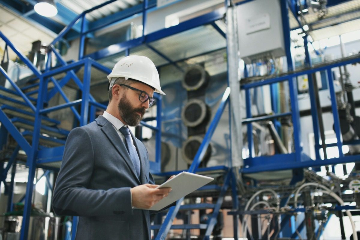 Man in a suit and glasses wearing a hard hat at a job site.