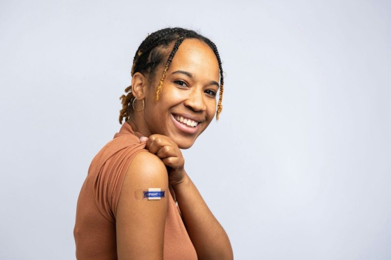 Black woman smiling and showing off the bandaid she got after receiving her vaccines.