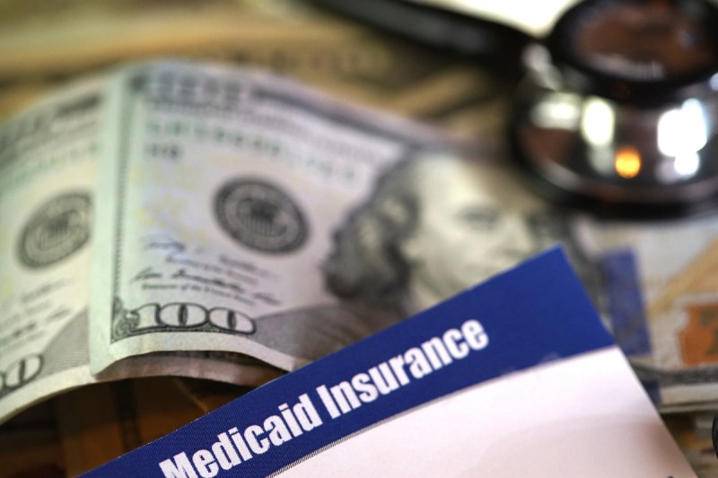 Medicaid healthcare insurance card in front of pile of money and stethoscope