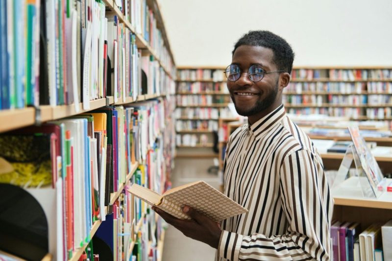 a man smiles while holding a book in a library