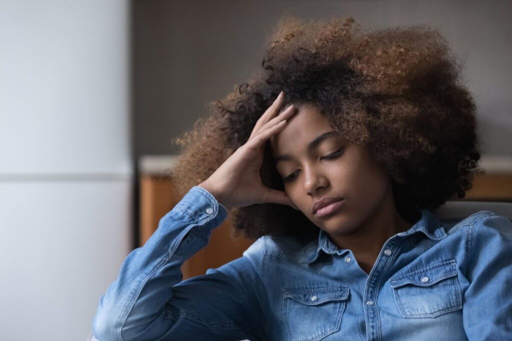 an african american girl with her head in her hands looks downward and depressed