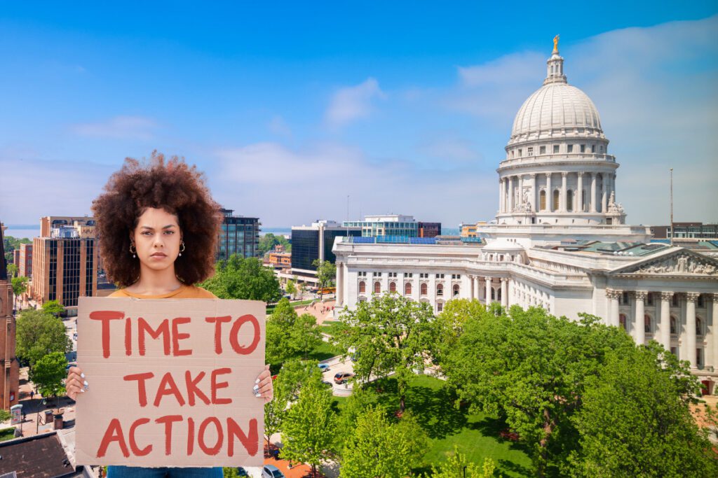 Photo illustration. Woman holding protests sign reading "time to take action". Madison Wisconsin in background