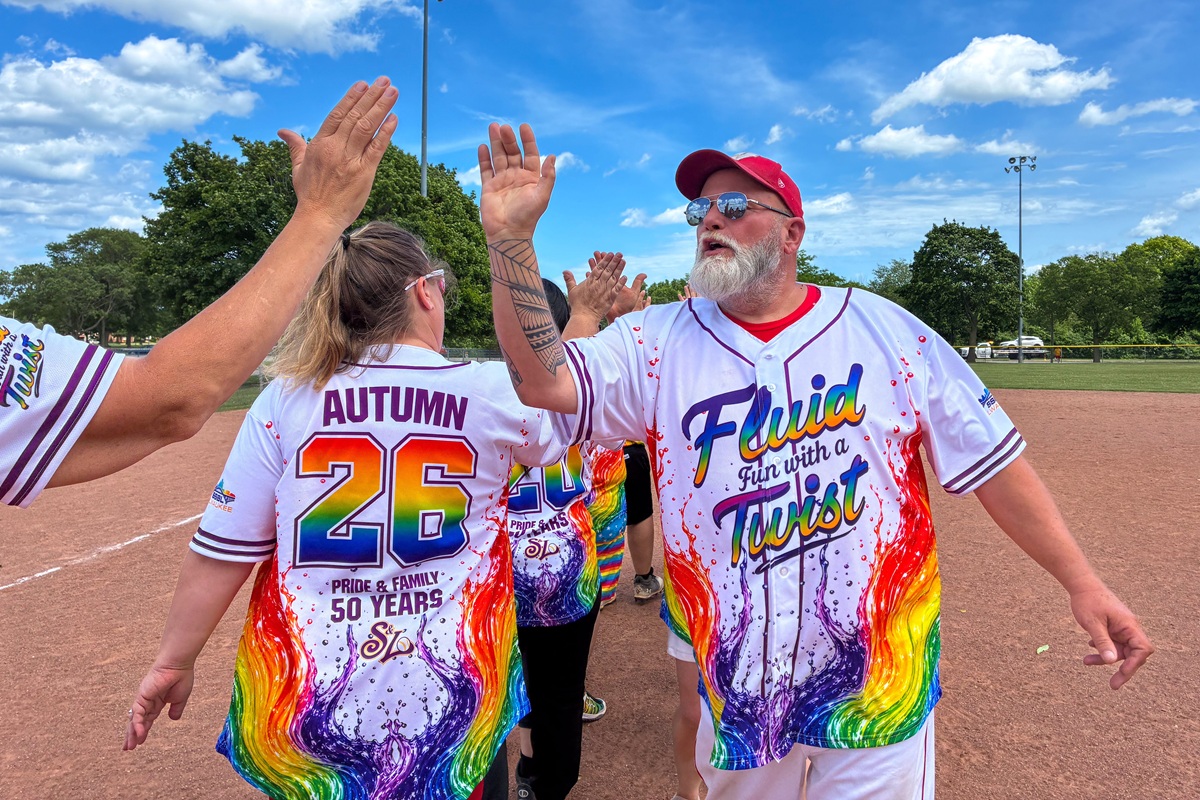 The commissioner of an LGBTQ softball league in Milwaukee wearing a rainbow-colored uniform slaps five with teammates